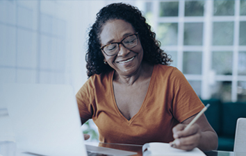 Person working at a desk, writing in a notebook while using a laptop.
