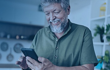 Person standing indoors and looking at a smartphone, with shelves and kitchen items visible in the background.