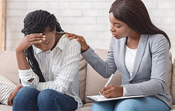 Woman receives emotional support from another woman while seated on a couch.