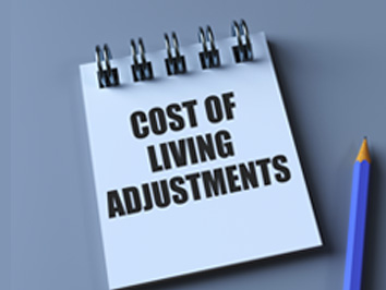 Spiral-bound notepad on a desk displaying the words “Cost of Living Adjustments,” with a pencil placed beside it.