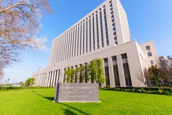 CalPERS headquarters building with a stone sign, green lawn, trees, and a clear blue sky.